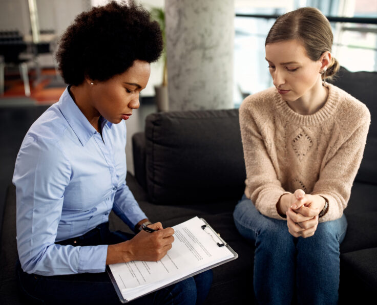 Black female counselor taking notes while having psychotherapy session with female patient.